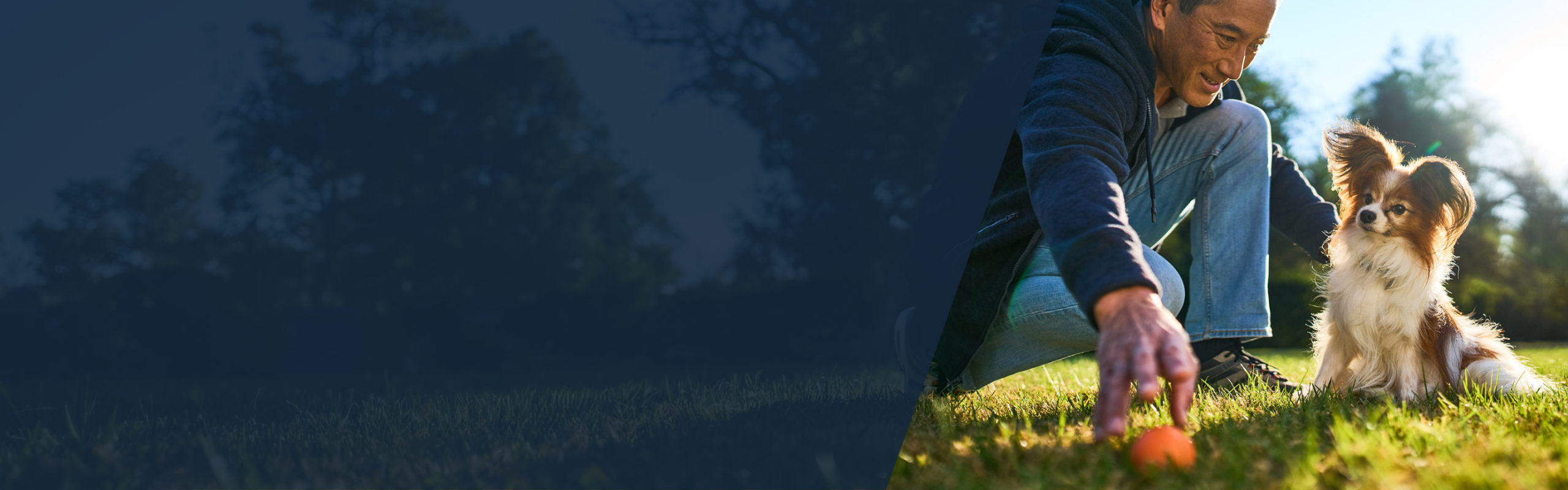 man playing ball in grass with small dog