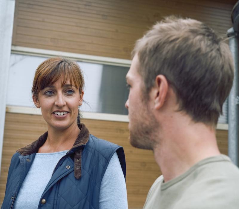 Poultry caretakers look at each other while having a conversation in front of a building